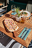 A beautiful wooden table with flatbread pizza, a glass of white wine and a platter of gourmet snacks in the warm daylight, perfect for al fresco dining