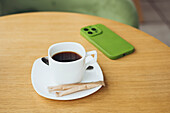 A cosy scene with a cup of coffee on a wooden table and a smartphone in a green case The simple, natural environment invites relaxation and concentration