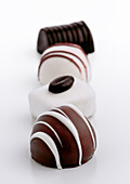 Various types of gourmet chocolate confectionery are arranged in a row on a white background. The chocolates feature intricate patterns and are made from both dark and white chocolate.