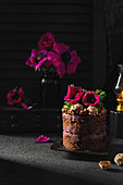 A rustic chocolate cake decorated with magenta-coloured anemone flowers against a dark background. The elegant composition is characterised by atmospheric lighting and floral accents.