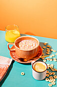 A lively breakfast tableau with a bowl of muesli with milk, a glass of orange juice and a cup of coffee against a colourful background.