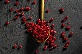 Top view of bright red peppercorns scattered by a golden spoon against a textured dark background showing vivid colour and texture contrasts in a gourmet setting.