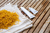 Marigold blossoms on a cloth next to white cosmetic tubes with marigold blossom cream on a wooden surface. The picture shows a natural, plant-based approach to skincare and beauty products.