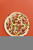 Top view of a gourmet pizza topped with roast beef, porcini mushrooms, cherry tomatoes, green onions and mozzarella cheese, beautifully presented on a warm colour background.