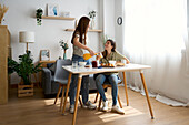 A warm scene shows a lesbian couple enjoying a delicious breakfast in their cosy dining room. The bright interior and natural light create a peaceful, loving atmosphere