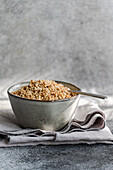 A rustic bowl filled with chopped hazelnuts, resting on a grey, textured cloth with an old spoon.