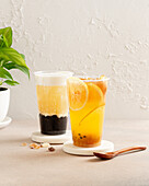 Two refreshing iced teas, one with lemon slices, the other with tapioca pearls, are elegantly served in clear glasses on coasters A green plant completes the scene