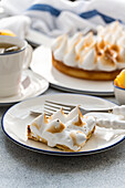 A slice of homemade lemon cake with toasted peaks on a plate, accompanied by a cup of tea. The scene captures a cosy dessert moment that is perfect for leisure or a get-together.