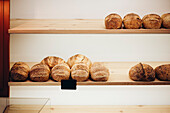 A selection of freshly baked, artisan bread, neatly arranged on wooden shelves in a cosy bakery The warm tones and rustic texture create a homely and inviting ambience