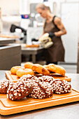 In einer belebten Bäckerei wird eine Vielzahl frisch gebackener italienischer Backwaren auf Holztabletts präsentiert Im Hintergrund bereitet ein Bäcker weitere köstliche Leckereien zu