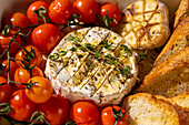 A delicious baked Camembert cheese, accompanied by fresh cherry tomatoes, roasted garlic and crispy slices of bread. Perfect for a gourmet starter or snack.
