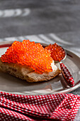 This close-up image shows healthy organic red caviar from trout fish generously arranged on a slice of crusty bread. The serving platter is accentuated by a decorative red and white dotted napkin, creating a visually appealing setting ideal for food presentations and culinary themes.