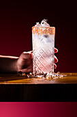 Ein kühler und erfrischender Paloma-Cocktail, garniert mit Chilipulver, steht auf einem Holztisch. Umgeben von Eis lädt er dazu ein, ein klassisches Getränk mit Zitrusgeschmack zu genießen