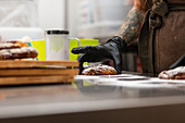 A skilful baker with tattooed arms and gloves arranges freshly baked pastries on a counter. The warm and inviting ambience reflects an authentic Italian bakery scene
