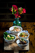 Bowls of chicken with glass noodles and peanuts, broccoli and cauliflower in satay sauce, tempura mushrooms in curry sauce and aubergine stew with rice