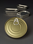 Close-up of various metal cans with hinged lids. These cans are stacked on a grey surface and show elements of industrial packaging design.