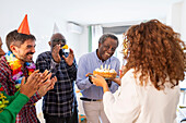 A group of people celebrate a birthday with smiles and clapping. One person presents a festive cake with lit candles, creating a cheerful and heart-warming atmosphere.