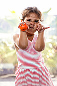 A child in a striped dress makes playful faces, holds a tangerine and enjoys a sunny day outdoors. The scene captures a moment of innocence and joy in summer.