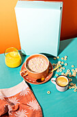 Top view of a lively breakfast scene with a bowl of cereal with milk, a cup of espresso and a glass of orange juice on a colourful background in turquoise and orange.