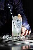 A tall, refreshing gin fizz cocktail in a clear glass filled with ice, elegantly garnished with a slice of citrus The drink rests on an elegant bar counter that exudes a chic and inviting atmosphere