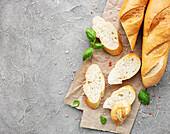Sliced fresh, crusty baguette with salt and basil on a grey concrete background