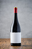 A single dark wine bottle with an empty label stands on a wooden surface against a soft grey background, ready for branding.