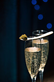 A spoonful of first-class Beluga caviar on a glass of champagne in front of a dark background with a subtle blue light.
