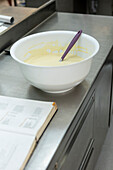 A mixing bowl with dough and a purple spatula on a stainless steel counter next to an open recipe book captures the essence of Italian baking