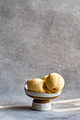 Three white Chinese pears on a ceramic plate against a textured grey background. The soft lighting and simple composition emphasise the natural elegance of the fruit.
