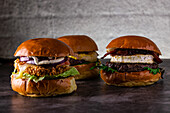 A delicious trio of gourmet burgers with unique toppings on a rustic wooden table. The selection includes crispy chicken, beef patty and grilled cheese, each with fresh ingredients.
