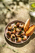A gourmet plate of baked snails, generously spread with melted butter and fresh parsley, accompanied by crispy, toasted slices of bread.