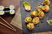 Top view of various sushi rolls on a dark slate. There are classic rolls and decorated rolls with colourful toppings.