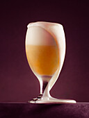 A close-up of an overflowing beer glass with a lush head of foam, taken against a dark background Perfect for illustrating beer, brewery or beverage themes