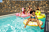 Eine fröhliche Familie entspannt sich in einem glitzernden Pool, umgeben von bunten aufblasbaren Schwimmern. Das helle Nachmittagssonnenlicht wirft spielerische Schatten auf das Wasser.