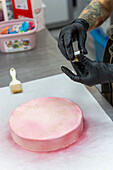A skilful baker with gloves applies pink icing and gold dust to a cake in an Italian bakery The process shows the craftsmanship and attention to detail typical of Italian bakeries