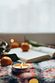 Warm and festive Christmas scene with a glowing candle, fresh oranges and an open book on a patterned blanket, conveying the joy and peace of the Christmas season.