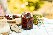 A rustic outdoor scene with a jar of homemade sun-dried tomatoes, fresh bread and ripe tomatoes on a wooden board. The warm, natural light emphasises the aesthetics of the farm and the food.