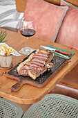 A delicious platter of sliced steak is served on a rustic wooden table, accompanied by crispy chips in a metal basket and a glass of red wine Cosy dining room ambience