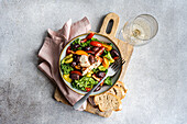 Top view of a salad with raw kale, various cherry tomatoes, red onion slices, grilled olives and seasoned feta cheese, artfully drizzled with olive oil. Served with slices of rustic bread and a glass of white wine.