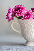 Beautiful pink flowers, elegantly arranged in a decorative white cup, standing on a lightly textured surface The soft colours and delicate blossoms create a cheerful atmosphere
