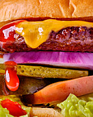 A stacked cheeseburger with beef patty, melted cheese, pickles, tomatoes, lettuce, red onions and ketchup - a delicious sandwich in close-up
