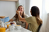 A lesbian couple enjoy breakfast together, exchanging smiles and affection. This heartwarming moment captures the essence of love and connection in everyday life