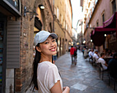 An Asian woman smiles as she walks through the picturesque cobbled streets of Volterra, Italy The historic charm of Tuscan architecture provides a beautiful backdrop