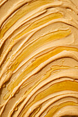 This close-up view from above shows the rich, smooth texture of creamy peanut butter drizzled with golden oil, highlighting its shiny, rippled surface.