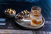 Spiced cognac cocktail with cinnamon and star anise, accompanied by almonds, peanuts and hazelnuts in rustic bowls on a textured tray.