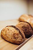 Close-up of freshly baked artisan bread resting on a rustic wooden shelf in a cosy bakery, highlighting crusty loaves with a golden texture