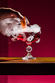 A Negroni cocktail in an elegant crystal glass, enhanced with a citrus garnish. The dramatic smoky effect adds a touch of mystery and elegance, perfect for a sophisticated bar or cocktail event
