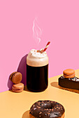 A delicious selection of coffee, macarons, a chocolate donut and a slice of cake on a bright pink and yellow background - ideal for brunch or breakfast