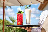 Two bright cocktails on a tray, including a red berry drink and a creamy pina colada. The shot was taken outdoors on a sunny day and embodies a tropical mood and refreshing flavours.