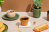 Cosy breakfast ambience with a cup of coffee, a plate filled with almonds and a sliced banana on peanut butter toast, surrounded by plants and warm decorative elements.